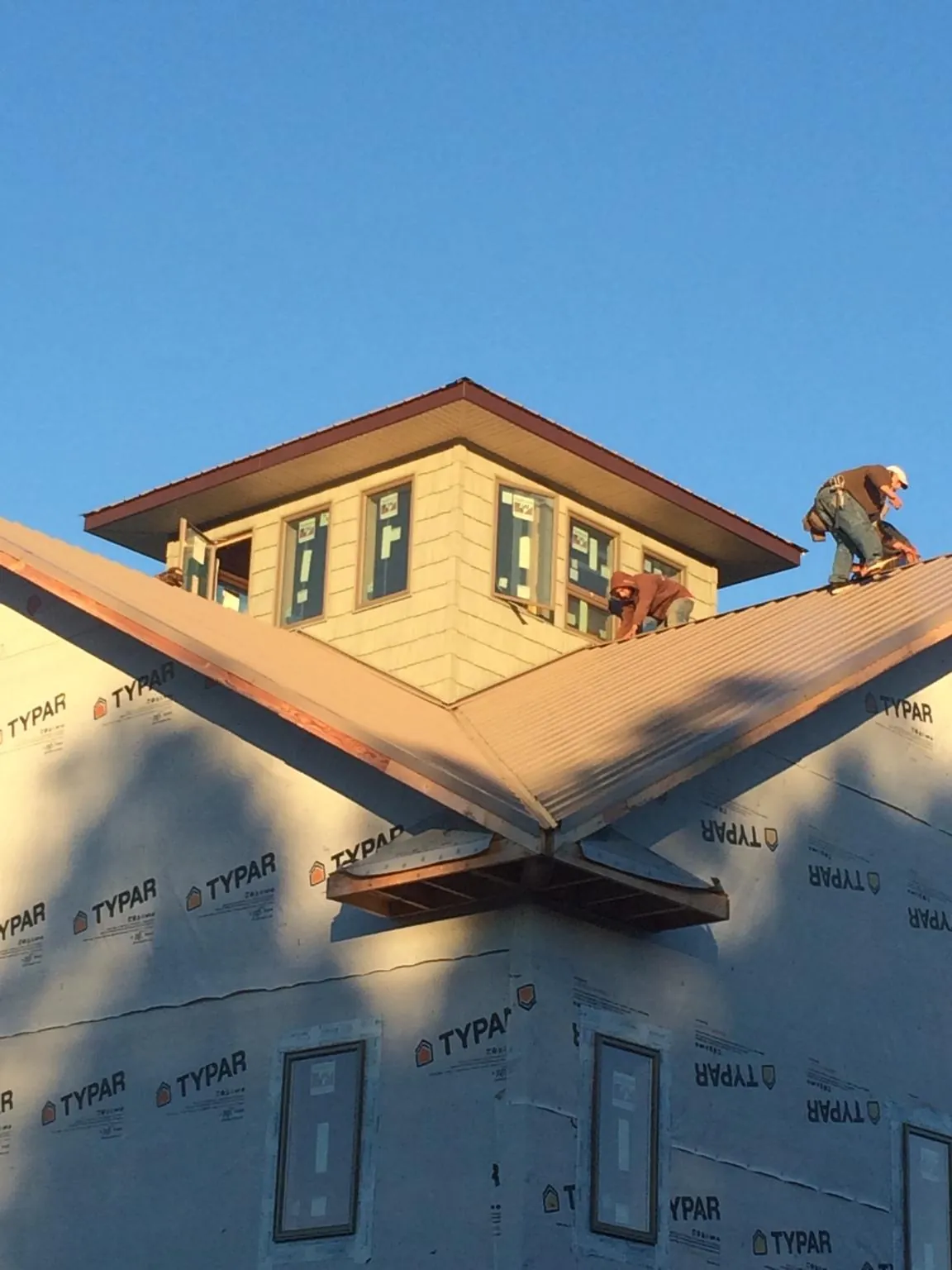 Roofers working around a rooftop cupola on a new metal roof at sunset in Phoenix